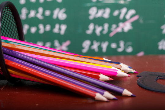 Colorful pencils of red yellow orange violet purple pink green and blue in stationary cup and ruler lying on brown school desk on written with white chalk blackboard backgroung on lesson of math