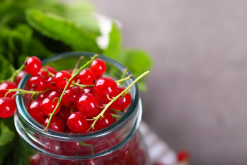 Fresh red currants in jar with mint on table close up