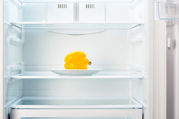 Yellow pepper on white plate in open empty refrigerator