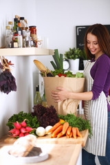 Young woman standing in her kitchen near desk with  grocery