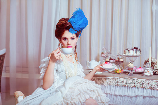 Indoors shot in the Marie Antoinette style. Woman drinking tea with sweets.
