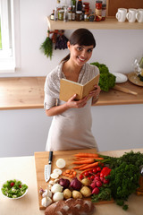 Young woman reading cookbook in the kitchen, looking for recipe