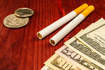 Couple of cigarettes with a several dollar bills and coins on th