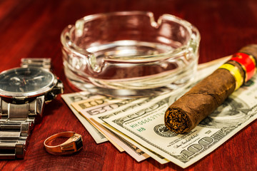 Cuban cigar with glass ashtray on a several dollar bills and gol - obrazy, fototapety, plakaty