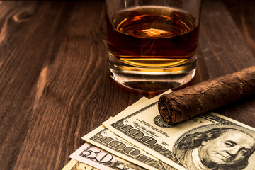 Glass of whiskey and a money with cuban cigar on a wooden table
