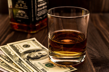 Glass of whiskey and bottle with money on a wooden table