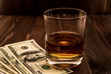 Glass of whiskey with money on a wooden table