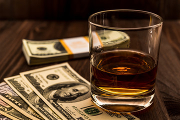Glass of whiskey with money on a wooden table