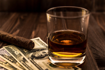 Glass of whiskey with a money and cuban cigar on a wooden table
