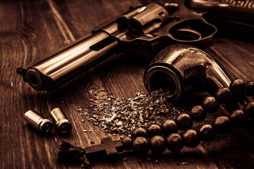 Revolver and a rosary with cross and tobacco pipe on a wooden table