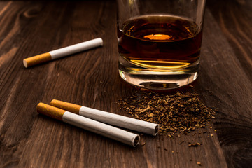 Glass of whiskey and three cigarettes with tobacco leaves on a wooden table