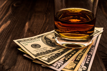 Glass of whiskey with money on a wooden table