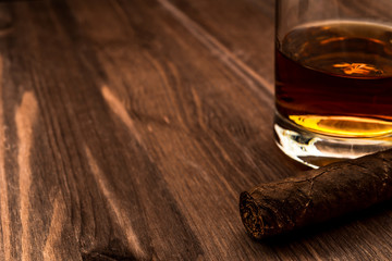Glass of whiskey and cuban cigar on a wooden table