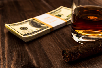 Glass of whiskey and a pack of dollars with cuban cigar on a wooden table