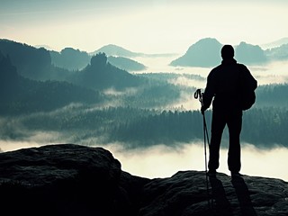 Dark silhouette of hiker with poles in hand. Sunny spring daybreak in rocky mountains. Hiker with...