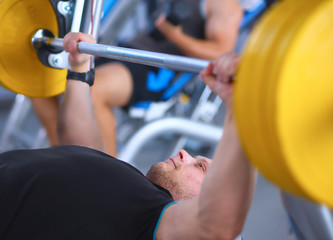 Fototapeta premium Young man lifting the barbell in gym with instructor