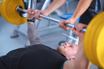 Fototapeta premium Young man lifting the barbell in gym with instructor