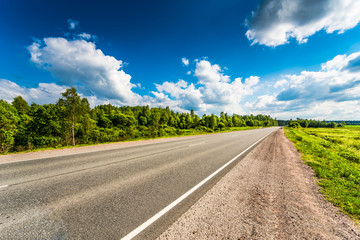 Rural road passing through fields and woods. View from the road