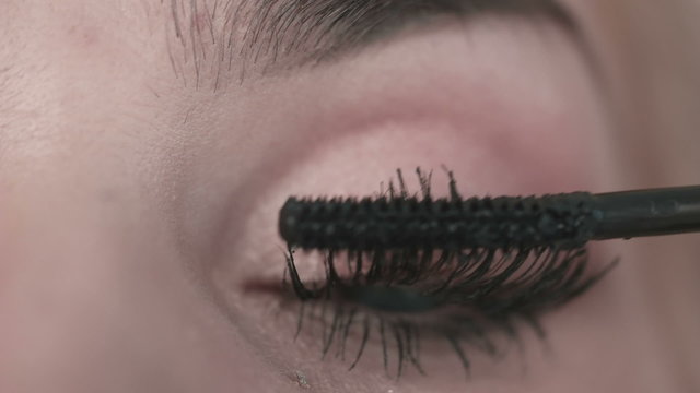 Eye in macro footage of young woman applying mascara on eyelashes