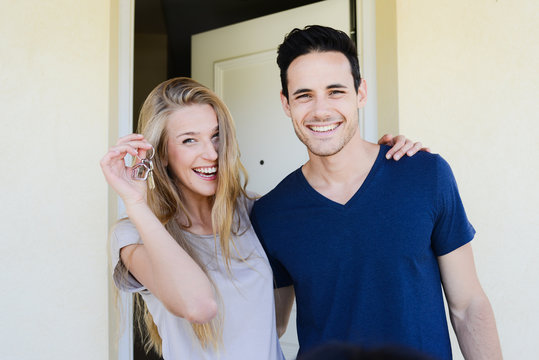 happy young couple man and woman handing their new home keys in front of an open house door