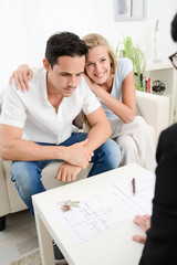 Obraz premium happy young couple at home with blueprint in discussion with a business woman