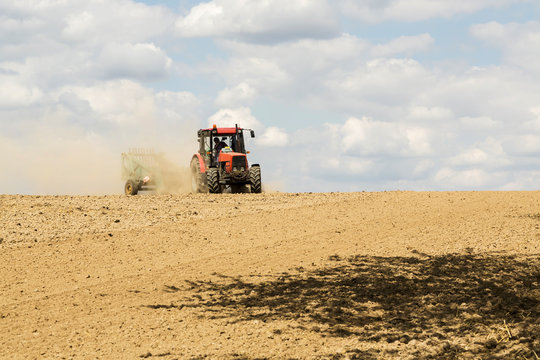 Tractor ploughing a field with a trail of dust behind it
