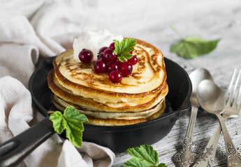 pancakes with honey, sour cream and red currants in a vintage scourage on a light wooden background