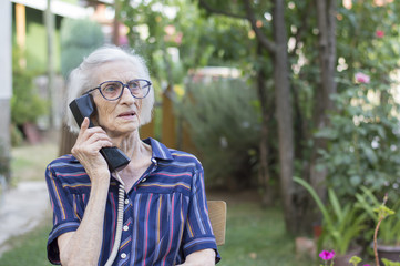Ninety years old lady talking on the phone in the backyard