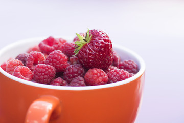 an orange cup filled with fresh raspberries and strawberry