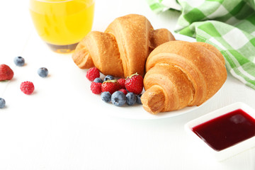 Fresh tasty croissants with berries on white wooden background