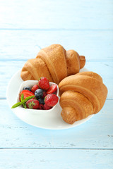 Fresh tasty croissants with berries on blue wooden background