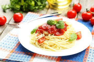 Spaghetti with tomatoes and basil on plate on grey wooden backgr