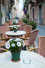 Fototapeta na wymiar Vase with white daisies on the table of a restaurant along the alleys in Ortigia, the old Syracuse