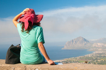 Tourist girl with a pink hat looking at the promontory of Mount Cofano from an elevated viewpoint...
