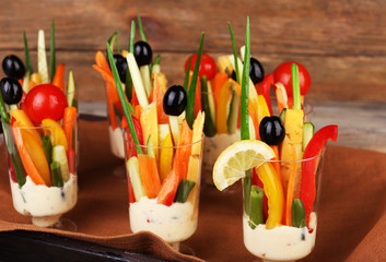 Snack of vegetables in glassware on tray on wooden background