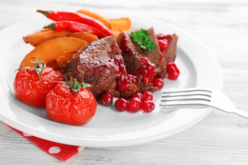 Tasty roasted meat with cranberry sauce and roasted vegetables on plate, on color wooden background