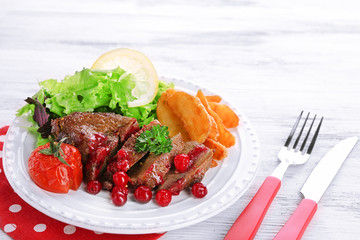 Tasty roasted meat with cranberry sauce and roasted vegetables on plate, on color wooden background