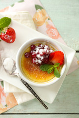 Creme brulee dessert with fresh strawberries and mint leaves, on color wooden background