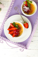 Creme brulee dessert with fresh strawberries and mint leaves, on color wooden background