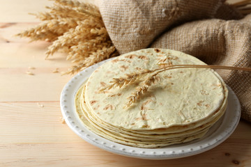 Stack of homemade whole wheat flour tortilla on plate, on wooden table background