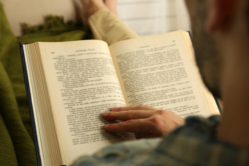 Young man reading book on sofa close up