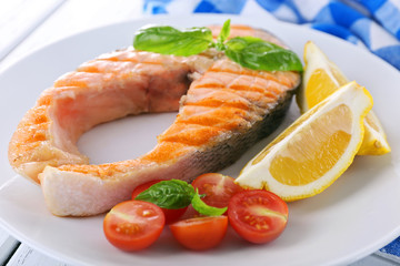 Tasty grilled salmon with tomato and lemon on table close up