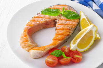Tasty grilled salmon with tomato and lemon on table close up