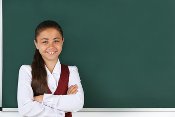 Beautiful little girl standing near blackboard in classroom