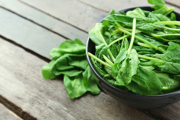 Bowl of fresh spinach leaves on wooden background