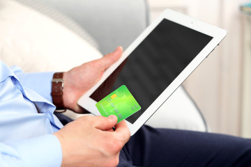 Man holding credit card and tablet on sofa in room