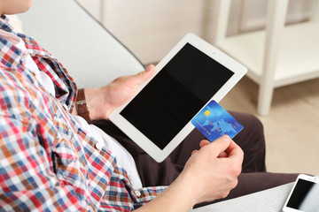 Man holding credit card and tablet on sofa in room