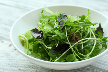 Fresh mixed green salad in bowl on wooden table close up