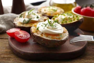Baked potato with mayonnaise and herbs on wooden cutting board, closeup