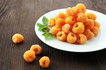 Yellow raspberries in white plate on wooden table, closeup